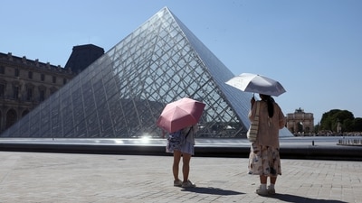 Tourists protecting themselves from the sun with umbrellas stand in front of the glass Pyramid of the Louvre museum as the museum closes early due to the heatwave as temperatures rise in Paris, France. (REUTERS)