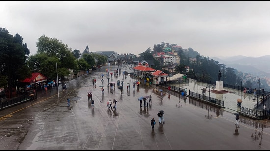 Tourists cover themselves with umbrellas as they walk amid rain on The Ridge in Shimla on Monday. (ANI Photo)