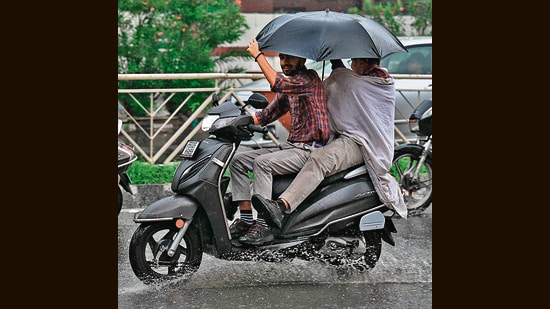 Scooterists carrying umbrella amid rainfall in Amritsar. (AFP)