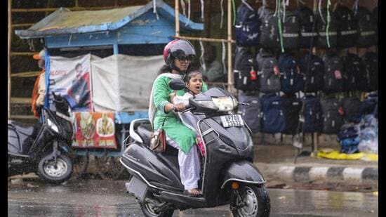 A woman and a child ride a scooter amid rain, in Prayagraj, on Wednesday. (PTI Photo)