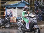 A woman and a child ride a scooter amid rain, in Prayagraj, on Wednesday. (PTI Photo)