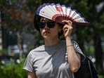 A woman uses a fan to shelter from the sun on a street in Seoul on July 12, 2026.