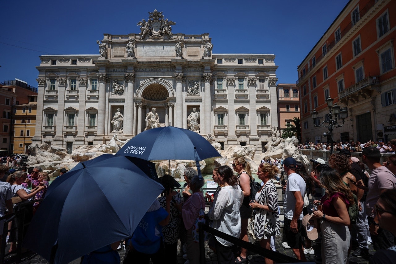 Tourists use umbrellas to shield themselves from the sun at the Trevi Fountain during a heat wave in Rome. Tourists use umbrellas to shield themselves from the sun at the Trevi Fountain during a heat wave in Rome.