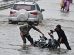 Two people struggle after their bike falls into a waterlogged stretch near Narsinghpur village on July 7 during the first official ‘heavy’ rain of the season. (Parveen Kumar/HT)