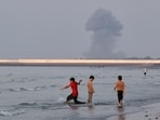 Three boys play in the shallow waters of the Strait of Hormuz, as a plume of smoke rises from an explosion in the background, off Bandar Abbas, Iran, Monday