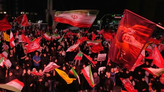 Pro-government demonstrators wave Iranian and religious flags in a gathering commemorating the late Iranian Supreme Leader Ayatollah Ali Khamenei, shown in a flag at right, at a square in Tehran, Saturday, July 11, 2026. (AP Photo/Vahid Salemi)