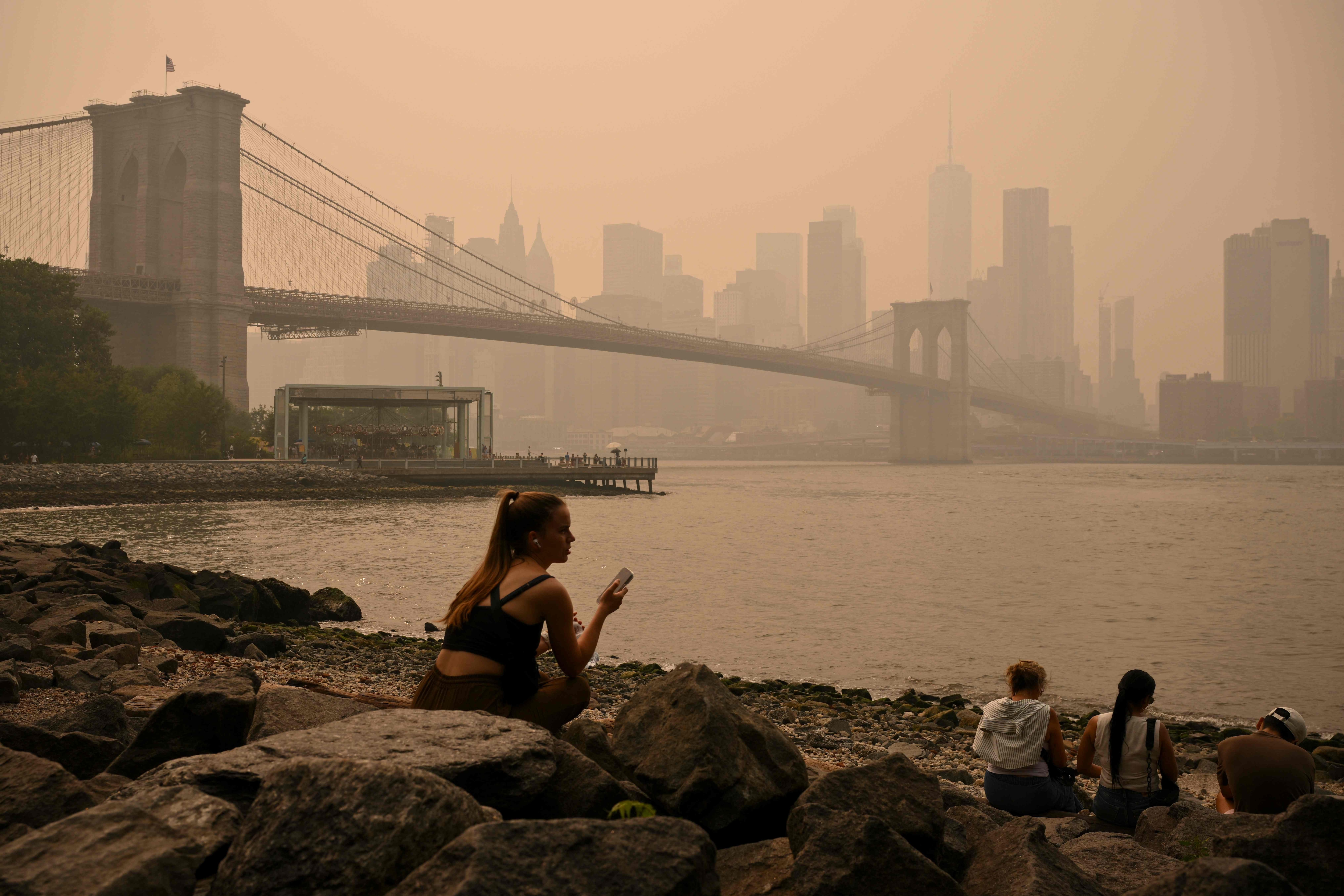 People sit near the Brooklyn Bridge as wildfire smoke from Canada causes hazy conditions in New York. (AFP) People sit near the Brooklyn Bridge as wildfire smoke from Canada causes hazy conditions in New York. (AFP)