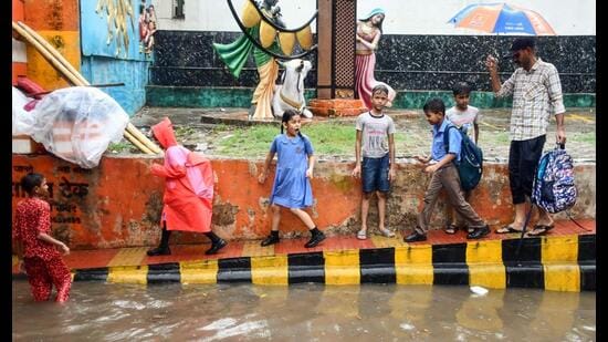 Children walk on a footpath beside a waterlogged road amid heavy rain, in Prayagraj on Monday. (ANI)