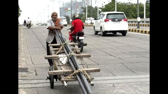 This humid evening, an elderly labourer is pushing a cart loaded with long iron pipes downhill a Central Delhi flyover. (HT Photo)
