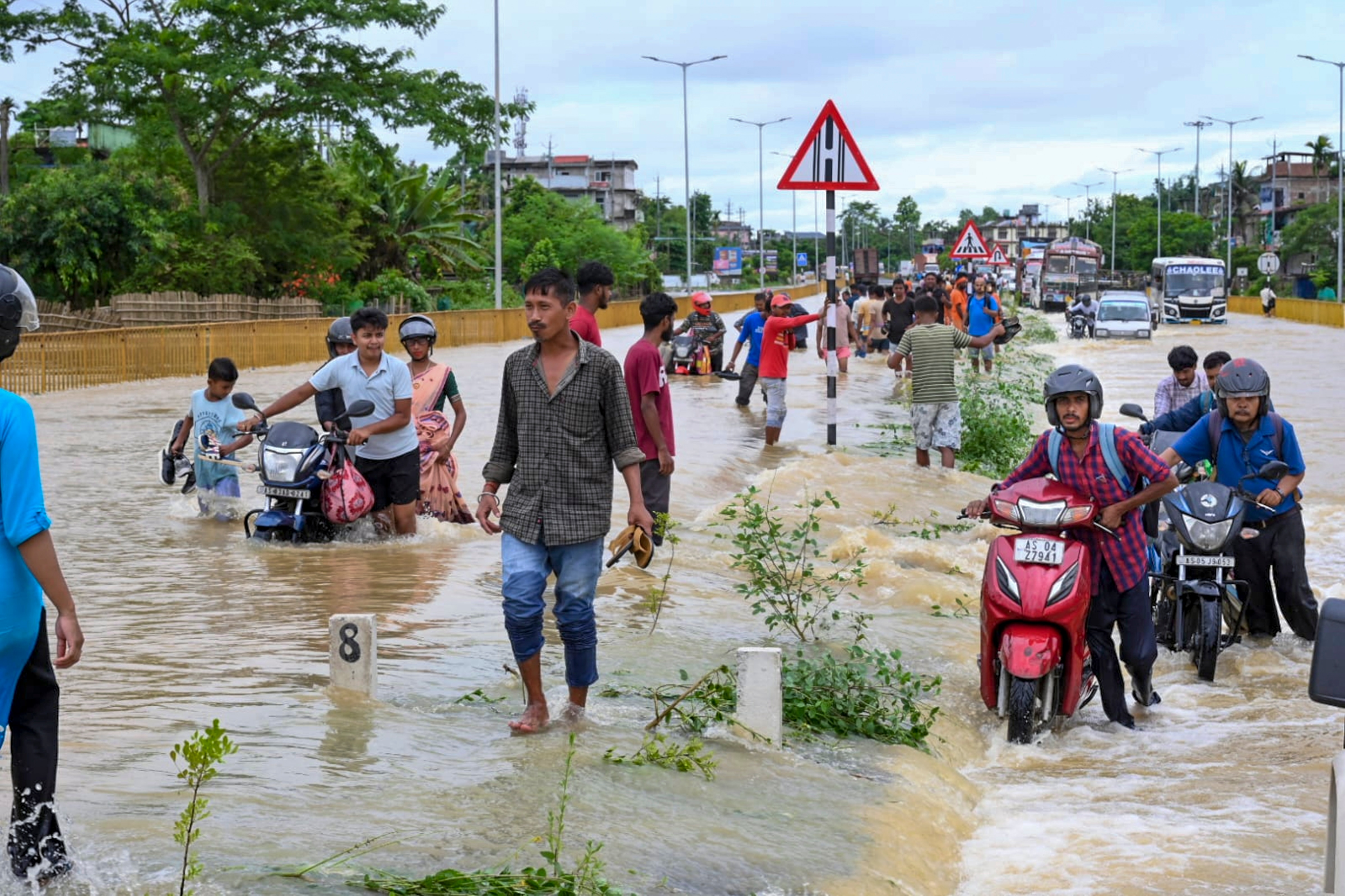 People wade through floodwaters and push two-wheelers along the submerged Jorhat-Sivasagar National Highway near Titabor, in Jorhat, Assam. (PTI) People wade through floodwaters and push two-wheelers along the submerged Jorhat-Sivasagar National Highway near Titabor, in Jorhat, Assam. (PTI)