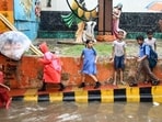 Children walk on a footpath beside a waterlogged road amid heavy rain, in Prayagraj on Monday. (ANI)