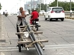 This humid evening, an elderly labourer is pushing a cart loaded with long iron pipes downhill a Central Delhi flyover. (HT Photo)