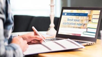 Young man writing college or university application form with pen and paper. Student applying or filling document. Scholarship, grant or admission. School website in laptop. (Getty Images/iStockphoto)