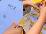 A woman opens a Blinkit packet containing protest posters.(X/@DocRGM_)