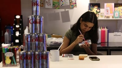 A woman uses rhinestones to decorate a Diet Coke can for an upcoming party to attract fans of the beverage amid an aluminium can shortage caused by disruption from the US and Israel's war with Iran, inside a cafe in New Delhi. (Reuters)