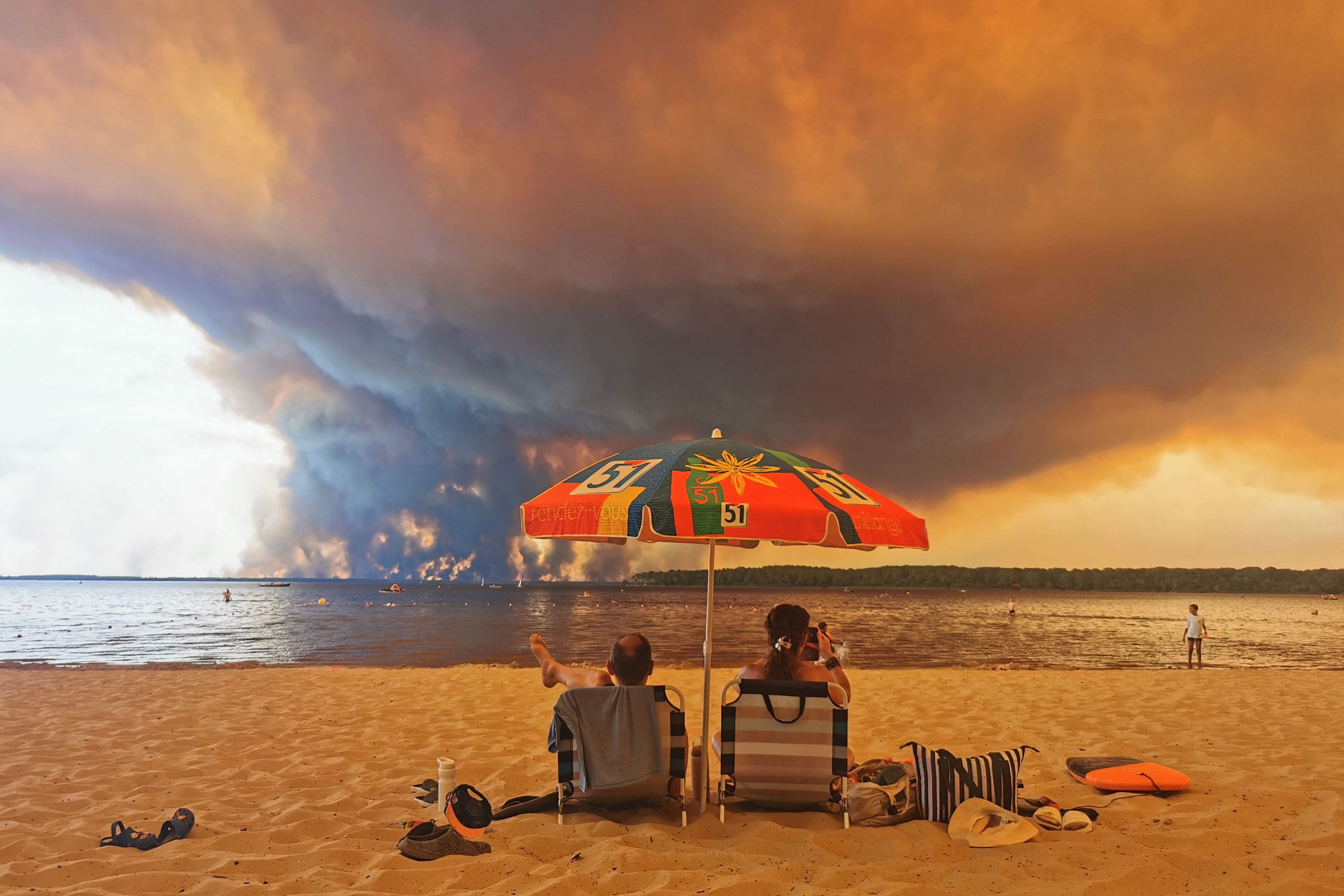 Beach goers sit on the beach of Moutchic in Lacanau, southwestern France, as clouds of smoke rise into the sky from a wildfire. (AFP)