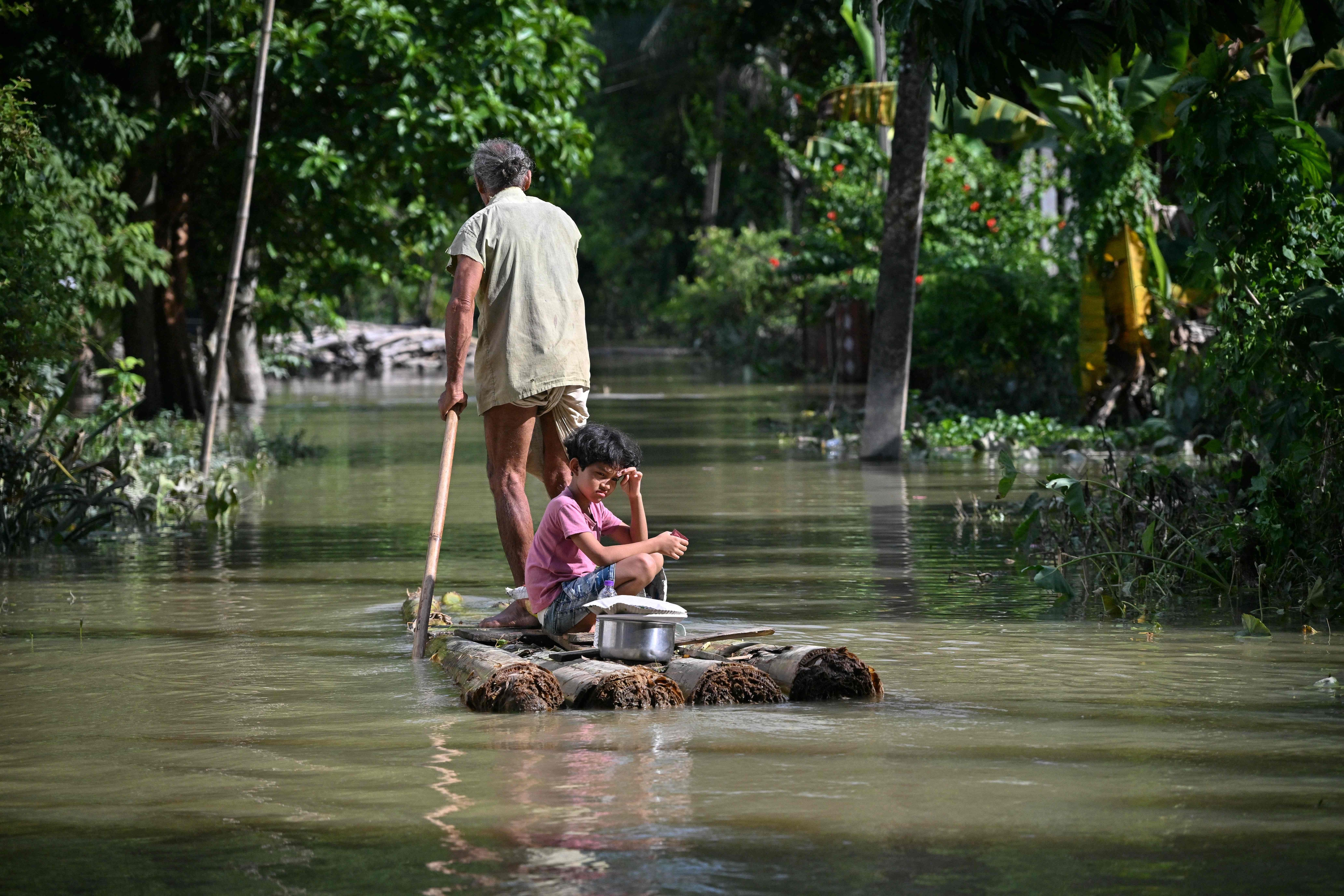 A girl and her grandfather travel on a raft through floodwaters following heavy monsoon rains at a village in Sivasagar district on July 27, 2026. (File Photo/AFP)