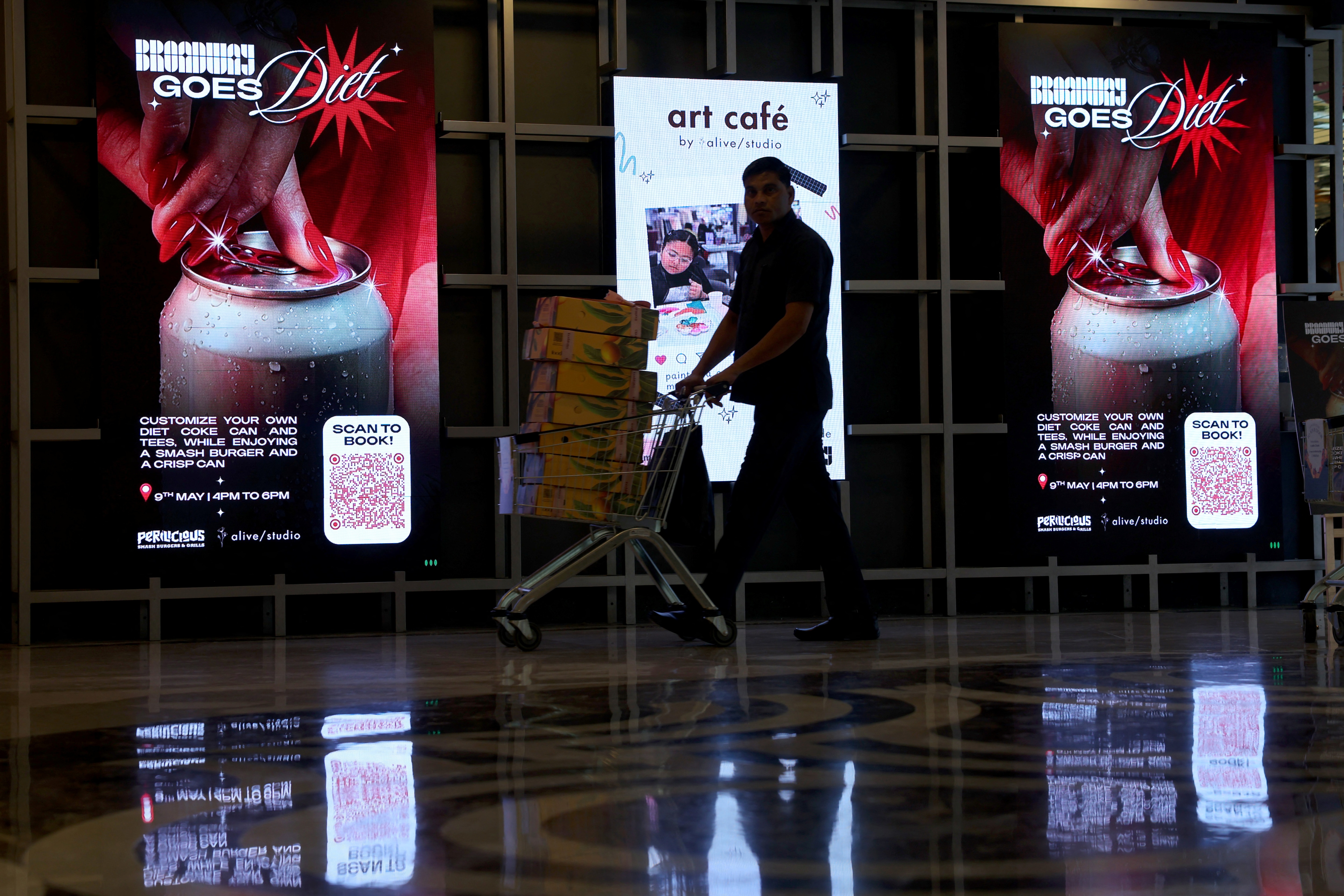 A man passes by screens displaying advertisements for an upcoming Diet Coke party, inside Art Cafe at Broadway store in New Delhi. (Reuters)