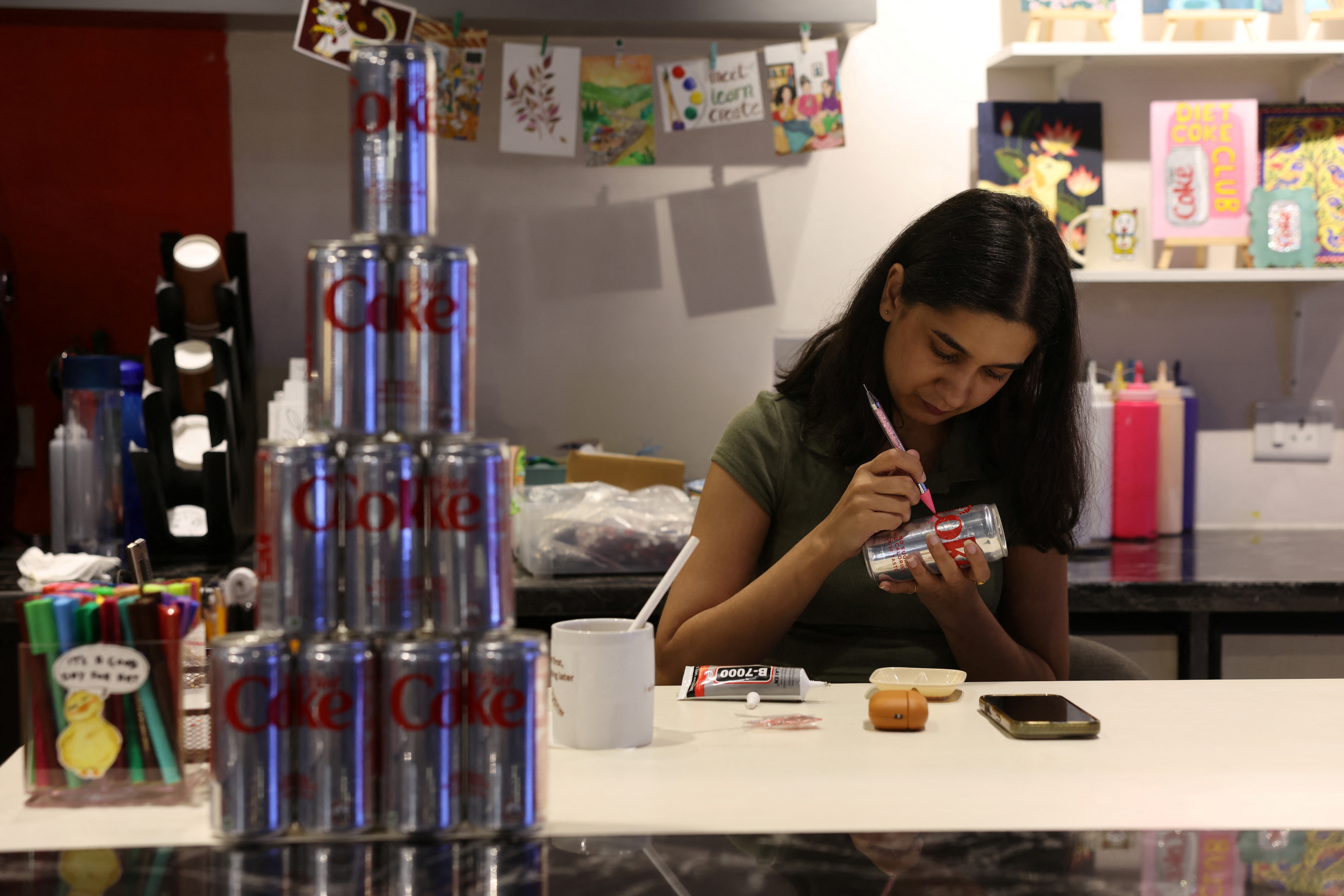 A woman uses rhinestones to decorate a diet coke can for a Diet Coke party to attract fans of the beverage amid an aluminium can shortage caused by disruption from the US and Israel's war with Iran, inside Art Cafe at Broadway store in New Delhi. (Reuters)
