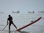 A man on a stand-up paddleboard as cargo ships and other commercial vessels appear anchored in the Strait of Hormuz off Bandar Abbas, Iran
