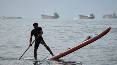 A man on a stand-up paddleboard as cargo ships and other commercial vessels appear anchored in the Strait of Hormuz off Bandar Abbas, Iran A man on a stand-up paddleboard as cargo ships and other commercial vessels appear anchored in the Strait of Hormuz off Bandar Abbas, Iran