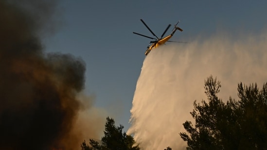 A firefighting helicopter drops water over a smoke-filled forest during a wildfire near Porto Germeno, northwest of Athens, Greece, Sunday, Aug. 2, 2026.