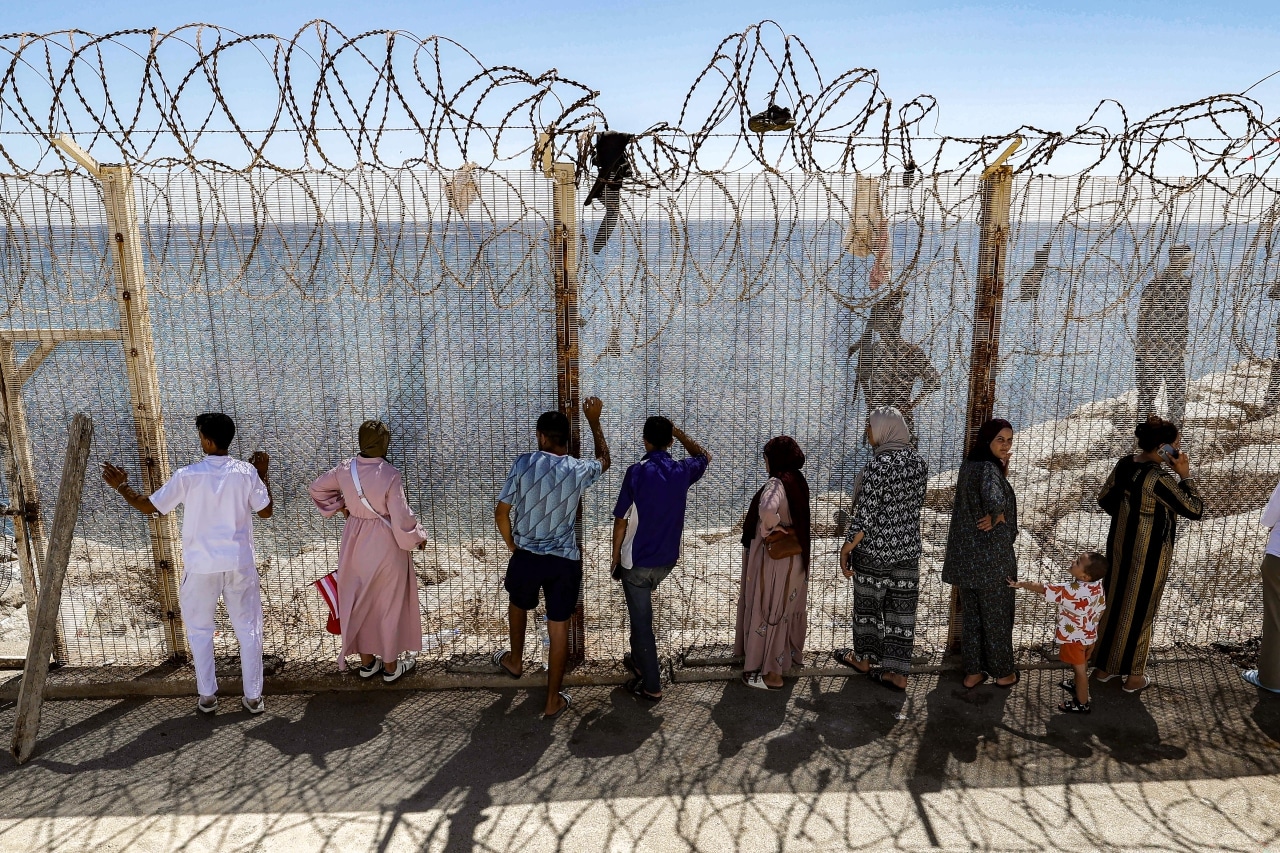 Relatives and friends wait by a fence topped with barbed-wire for the return of people who had crossed into Ceuta. Relatives and friends wait by a fence topped with barbed-wire for the return of people who had crossed into Ceuta.