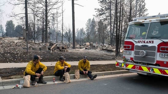 Three members of the Spokane Fire Department sit on a curb in front of burned-out residential homes in the Balboa neighborhood of Spokane, Washington, on August 2, 2026.  (Photo by Erick Doxey / AFP)