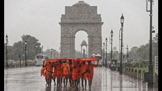 Kanwariyas shield themselves from heavy rainfall at India Gate in New Delhi. (PTI)