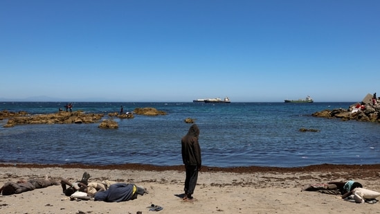 A migrant prays and other rest while waiting on the beach following mass crossings of migrants on foot and by sea from Morocco into Spanish territory, in Ceuta, Spain, August 4, 2026.