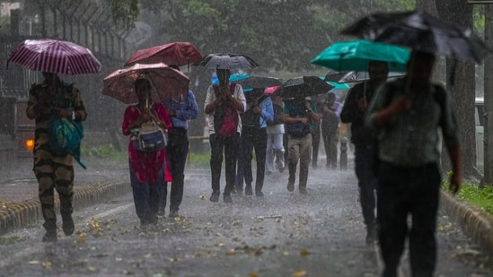 Weather today LIVE updates: Commuters walk on a road amid heavy rain, in New Delhi. Weather today LIVE updates: Commuters walk on a road amid heavy rain, in New Delhi.