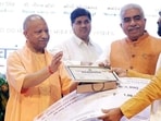 Chief minister Yogi Adityanath hands over a certificate and award cheque to a handloom artisan during the National Handloom Day programme, in Lucknow on Friday. (@myogiadityanath X/ANI Photo)