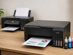 A refillable ink tank printer beside a traditional cartridge printer with printed documents.