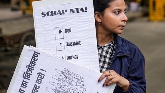 A demonstrator holds placards during a protest against the police crackdown on students and youth over the NEET paper leak issue, at Jantar Mantar.