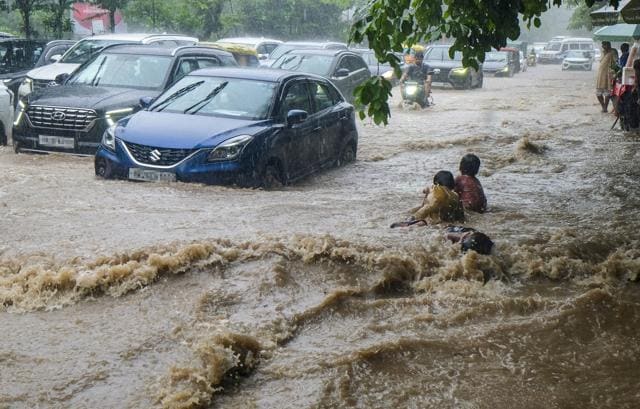 Vehicles wade through a flooded stretch in Sector 38 as children play along the road. (PTI) Vehicles wade through a flooded stretch in Sector 38 as children play along the road. (PTI)