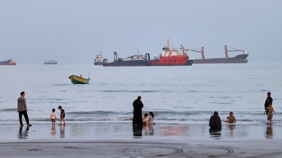 People spend time at a beach as commercial vessels are anchored in the Strait of Hormuz off Bandar Abbas, Iran.