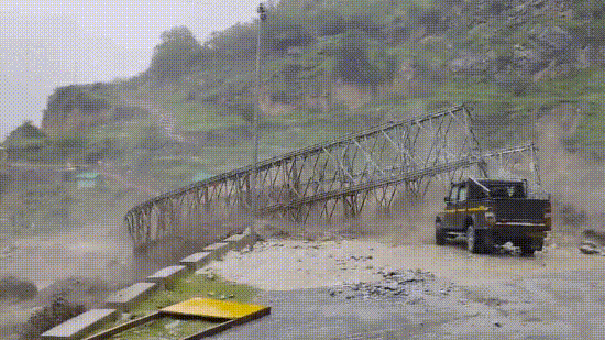 A video of the incident shows a powerful surge of muddy water rushing through the valley and hitting the metal bridge.