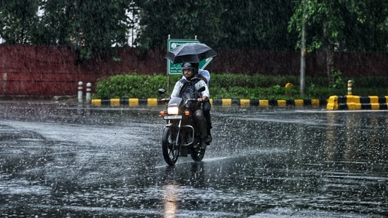 A commuter on a two-wheeler passes through a rain-slicked road amid heavy rainfall, in New Delhi.