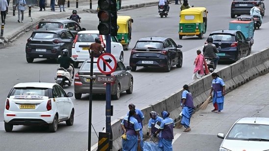 File image: Sanitation workers clean a roadside median as traffic moves along a road in Bengaluru