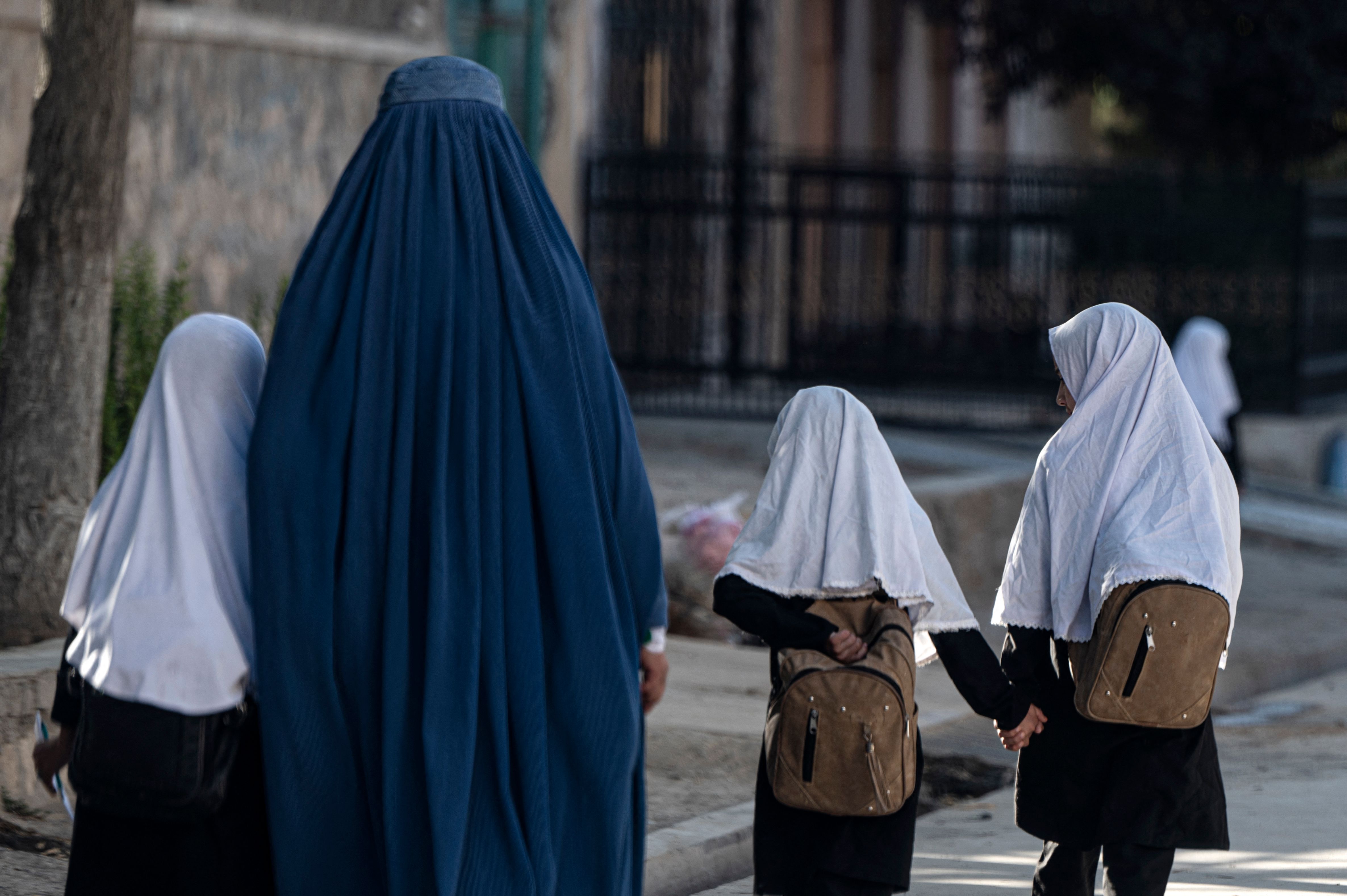 This photograph taken on August 9, 2022 shows an Afghan woman walking with schoolgirls going to their primary school in Kabul. (AFP)
