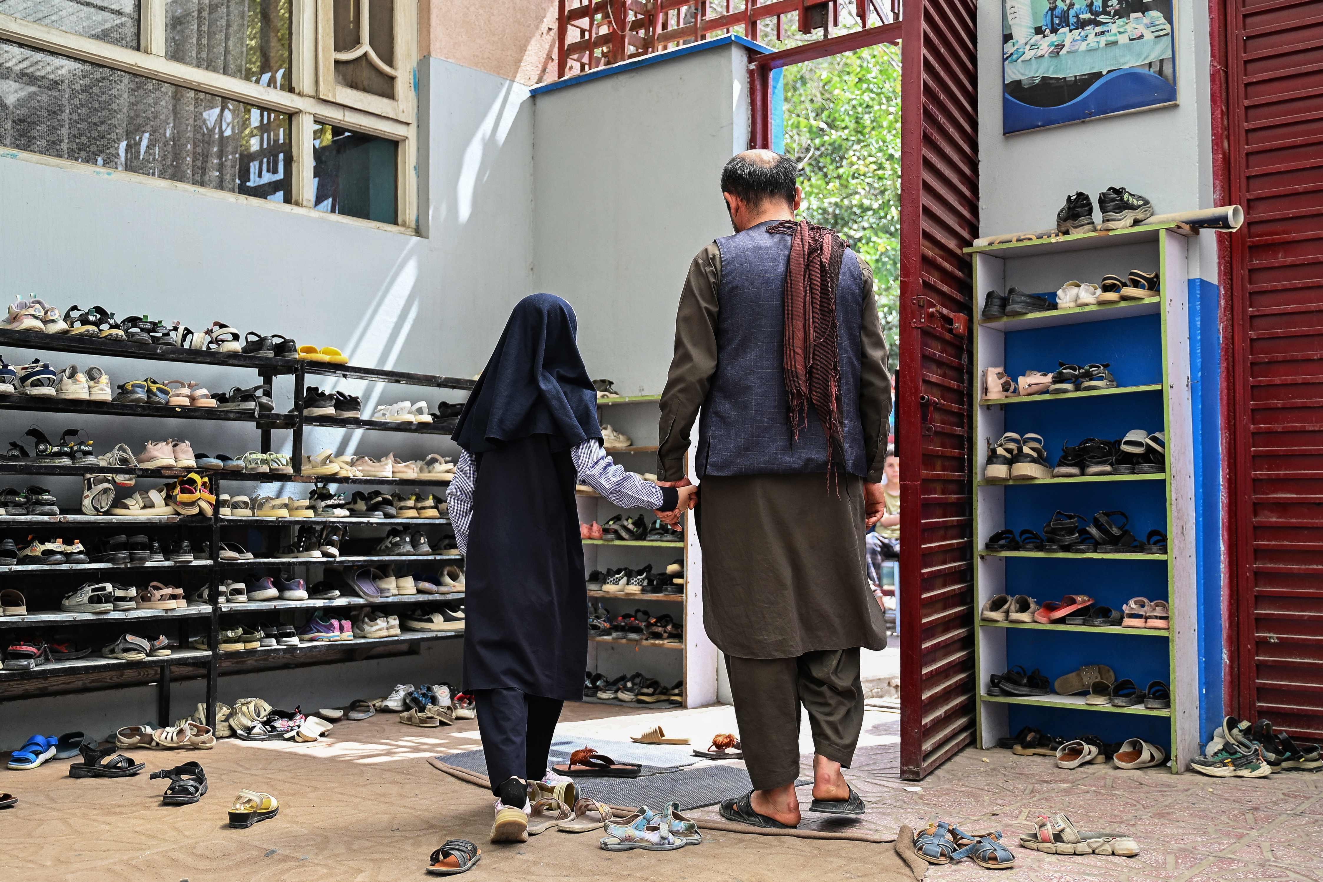 This photograph taken on July 21, 2026 shows an Afghan schoolgirl holding her father's hand leaving after taking a midterm exam at a primary school in Kabul. (AFP)