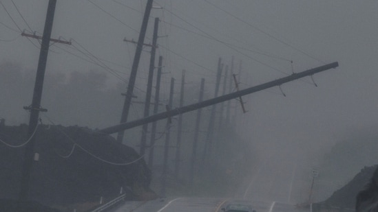 A vehicle drives near a downed utility pole dangling above Mamalahoa Highway during Hurricane Lala near Ocean View, Hawaii.