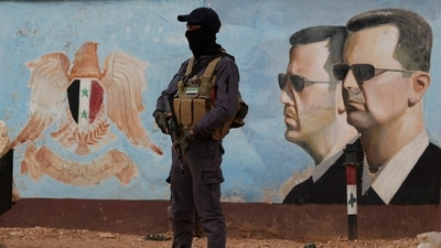 A member of the former rebel group Hayat Tahrir al-Sham stands guard near an image of Syria's Bashar al-Assad at the fourth division headquarters in Damascus, Syria. (File Photo/Reuters)