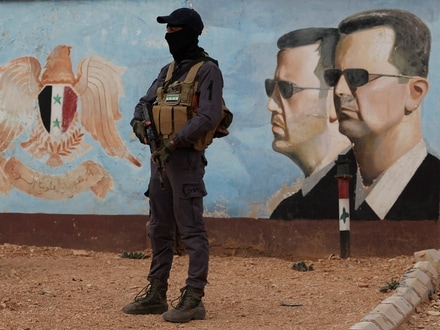 A member of the former rebel group Hayat Tahrir al-Sham stands guard near an image of Syria's Bashar al-Assad at the fourth division headquarters in Damascus, Syria.