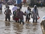 People wade through a waterlogged road along the banks of the swollen Ganges as the river's water level rises following heavy rainfall, in Prayagraj on Wednesday. (PTI)