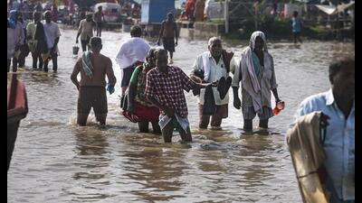 People wade through a waterlogged road along the banks of the swollen Ganges as the river's water level rises following heavy rainfall, in Prayagraj on Wednesday. (PTI)