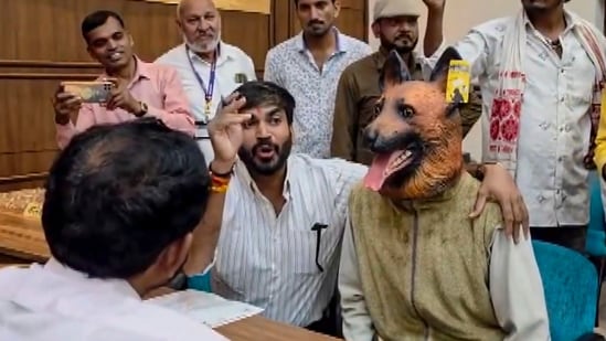 Khandwa Municipal Corporation Leader of Opposition Deepak Mullu Rathore argues with a municipal official while a supporter dressed in a dog costume sits beside him
