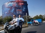 Motorcyclists pass a billboard depicting U.S. President Donald Trump underwater amid explosions, with the words 