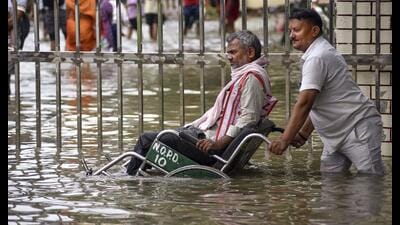 A man assists a person in a wheelchair through a waterlogged area after heavy rain, at BHU Hospital, in Varanasi on Tuesday. (PTI)