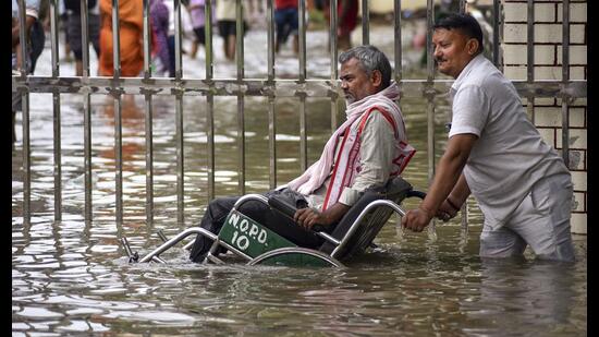 A man assists a person in a wheelchair through a waterlogged area after heavy rain, at BHU Hospital, in Varanasi on Tuesday. (PTI)
